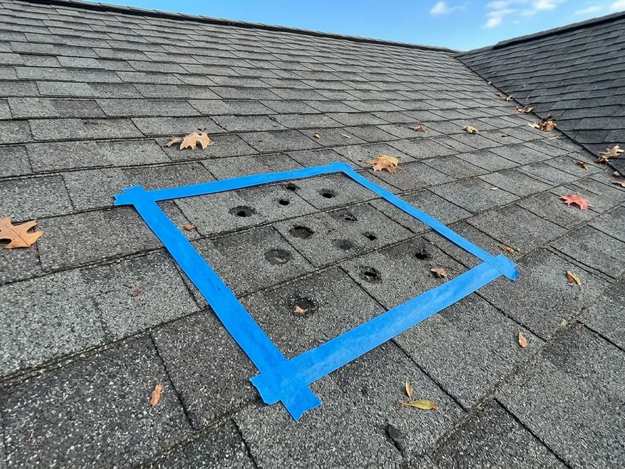 Square outlined with blue painter's tape on a weathered asphalt shingle slope with small hail marks inside it, seen from above
